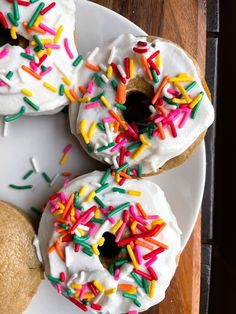 three donuts with white frosting and colorful sprinkles on a plate