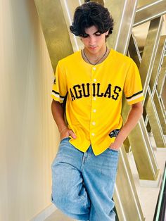 a young man in a yellow baseball jersey leaning against a metal wall with his hands on his hips