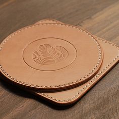 two tan leather coasters sitting on top of a wooden table next to each other