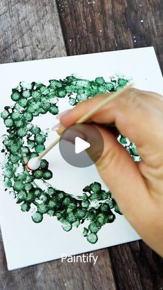 someone is painting a wreath with green paint on white paper and holding a pencil in their left hand