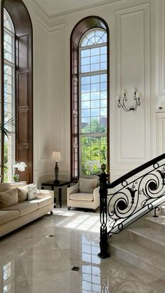 a living room filled with white furniture and two large windows next to a stair case