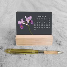 a desk calendar and pen sitting on top of a wooden block next to a marble surface