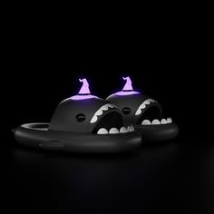 two black objects with white teeth and purple lights on their heads are sitting in the dark