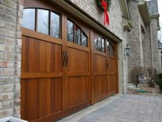 a large wooden garage door in front of a brick house with wreaths on it