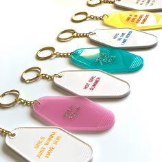 six key chains with different colored tags attached to them on a white surface, one has a gold chain and the other is blue