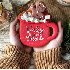 a person holding a red mug with a gingerbread in it and the words baby, it's cold outside