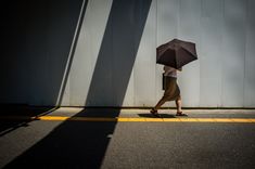 a person walking down the street with an umbrella in their hand and shadows on the wall behind them