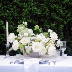 a table with white flowers and silverware on it is set for an elegant dinner