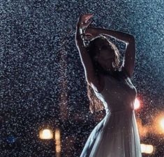 a woman is standing in the rain with her arms up and hands behind her head