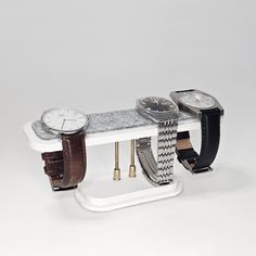 three watches are sitting on top of a white shelf with two leather straps around them