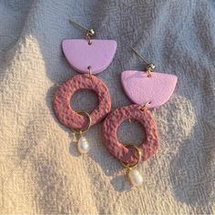 two pairs of pink and purple earrings on a white sheet with pearls hanging from them