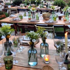 the table is set with many vases and glasses on it, along with candles