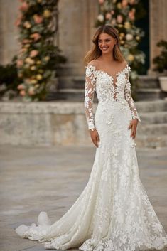 a woman in a white wedding dress standing on a stone floor with flowers behind her