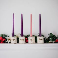 four candles with words on them sitting in front of flowers and greenery next to a fireplace