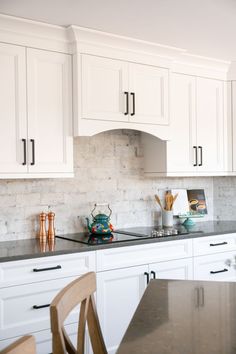 a kitchen with white cabinets and marble counter tops, along with a wooden dining table