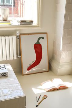 an open book sitting on top of a table next to a red chili pepper poster