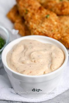 a white bowl filled with dipping sauce next to fried chicken strips and green vegetables on a napkin