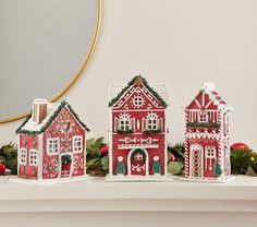 three red and white gingerbread houses sitting on top of a mantle next to christmas decorations