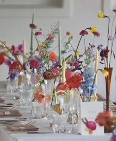 there are many flowers in the vases on this long table with place card holders