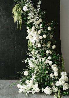 white flowers and greenery are arranged on the floor in front of a black wall