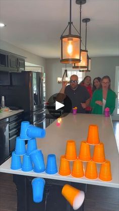 a group of people standing around a kitchen table with cups on it and an orange cone in the middle