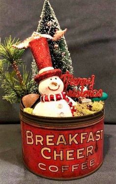 a snowman in a red hat is sitting in a coffee can with the words breakfast cheer on it