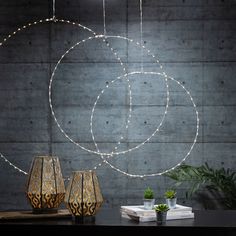 three vases sitting on top of a table next to a wall with lights hanging from it