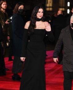 a woman in a black dress walking down a red carpeted area with other people