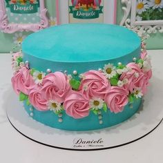 there is a blue cake with pink flowers on top and pearls around the edges, sitting on a table