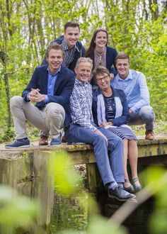 a group of people sitting on top of a wooden bridge in the woods with trees behind them