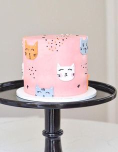 a pink cake with cats on it sitting on top of a black stand in front of a white wall