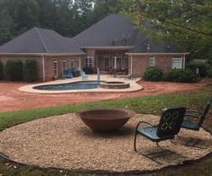 a backyard with a fire pit and lawn furniture in the foreground, surrounded by trees