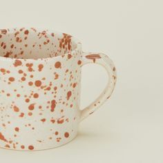 an orange and white speckled coffee cup on a white surface with brown spots in it