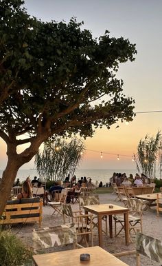 an outdoor dining area with tables and chairs on the beach at sunset or dawn,