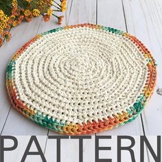 a crocheted round rug on a white wooden floor with flowers in the background