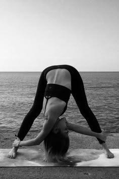 a woman doing a handstand on top of a mat next to the ocean