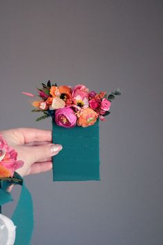 a person holding a green box with flowers in it's center and a napkin hanging from the side