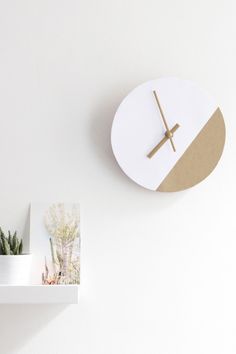 a clock mounted to the side of a white wall next to potted plants and cacti