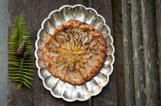 a pie sitting on top of a metal pan next to a green fern leaf and pine cone