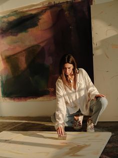 a woman kneeling on the floor in front of a painting