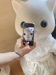 a person holding up a cell phone to take a picture of a stuffed animal cat