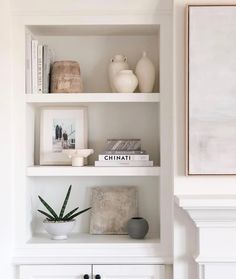 a white book shelf with books and vases on it, along with other items