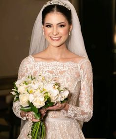 a woman in a wedding dress holding a bouquet of flowers and smiling at the camera