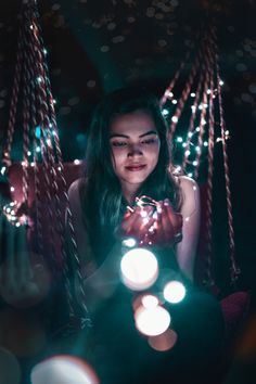 a woman sitting on a swing with lights in her hands and looking at the camera