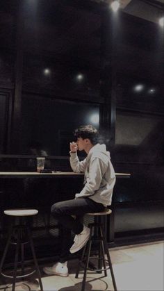 a young man sitting at a bar drinking from a cup with his hand up to his mouth