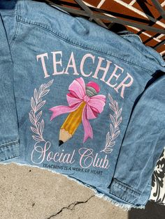 a jean jacket with a pink bow on it and the words teacher social club painted on it