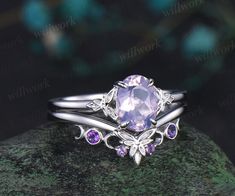 a ring with an amethorate stone and purple stones on the side, sitting on top of a rock