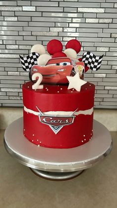 a red cake decorated with cars and mickey mouse ears on top of a silver platter