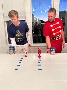 two men standing at a table with legos in front of them and one is wearing a red shirt