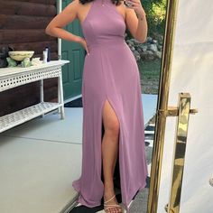 a woman standing in front of a mirror wearing a purple dress with high slits